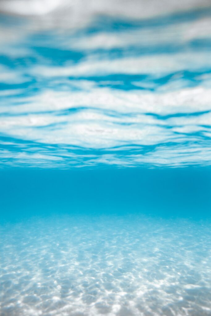 Serene underwater scene with clear blue water and light reflections on sandy ocean floor wallpaper