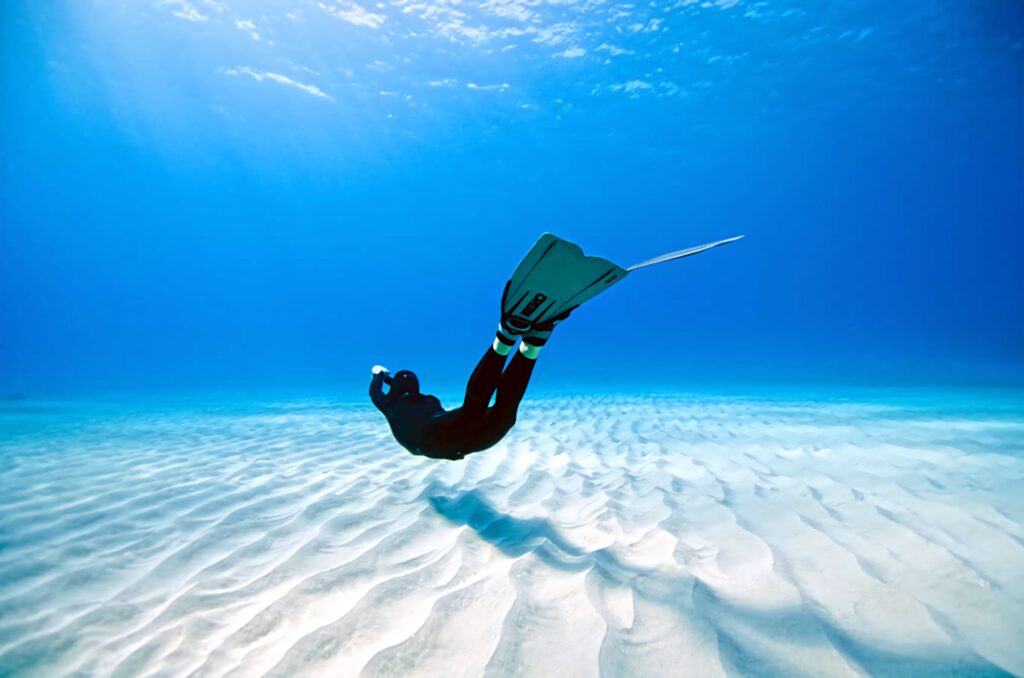 Lone diver gliding over rippled ocean floor under clear blue water with sunlight rays wallpaper
