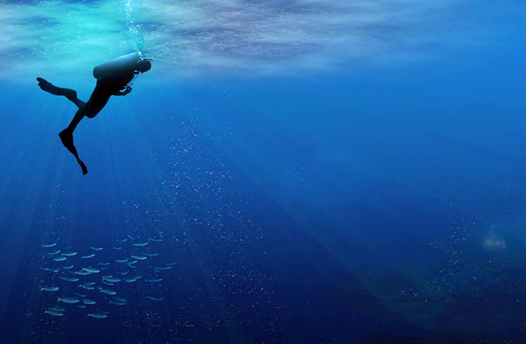 Scuba diver swimming in clear blue sea with sunlight rays and distant school of fish wallpaper