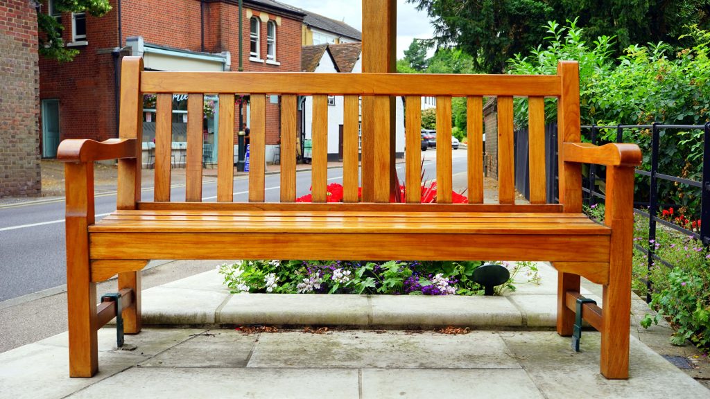 Classic wooden bench by colorful flower garden on paved sidewalk with brick building background Wallpaper