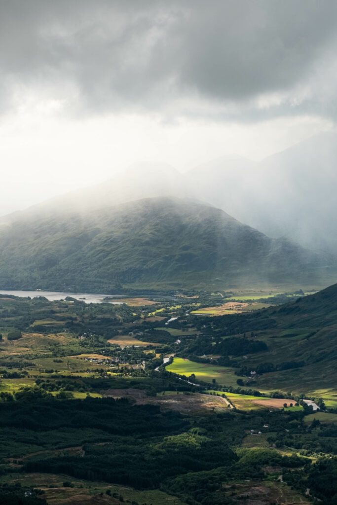Breathtaking valley with lush green fields quaint houses misty mountains and soft sunlight wallpaper