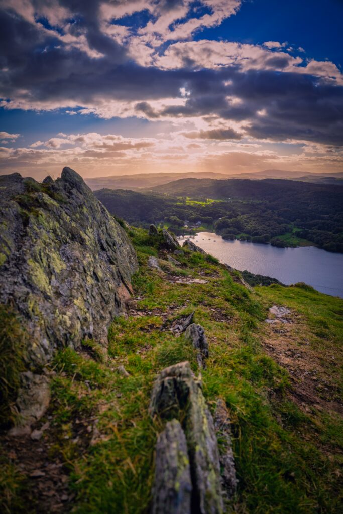 Serene valley wallpaper with rugged rocks green hills and lake reflecting dramatic sky sunlight