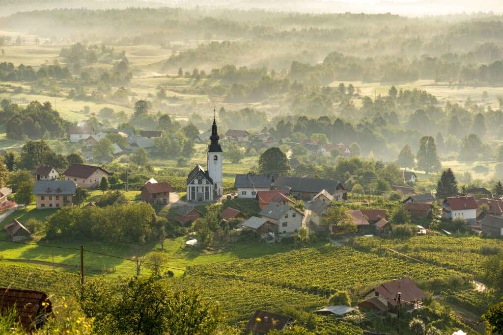Serene valley with quaint houses chapel soft morning fog golden light lush green fields wallpaper