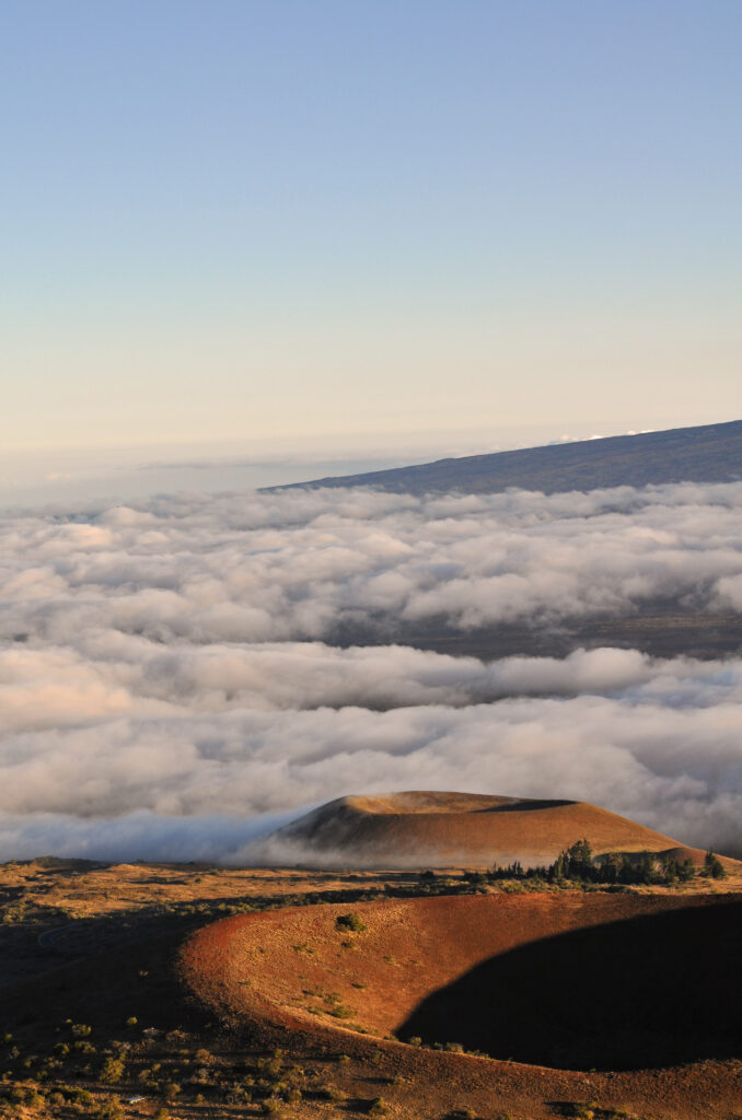 Volcanic crater with rugged terrain and soft clouds under clear blue sky natural wallpaper background