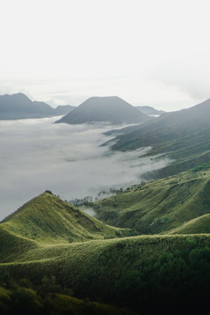 Serene volcanic landscape with green mountains and foggy clouds creating a tranquil atmosphere Wallpaper