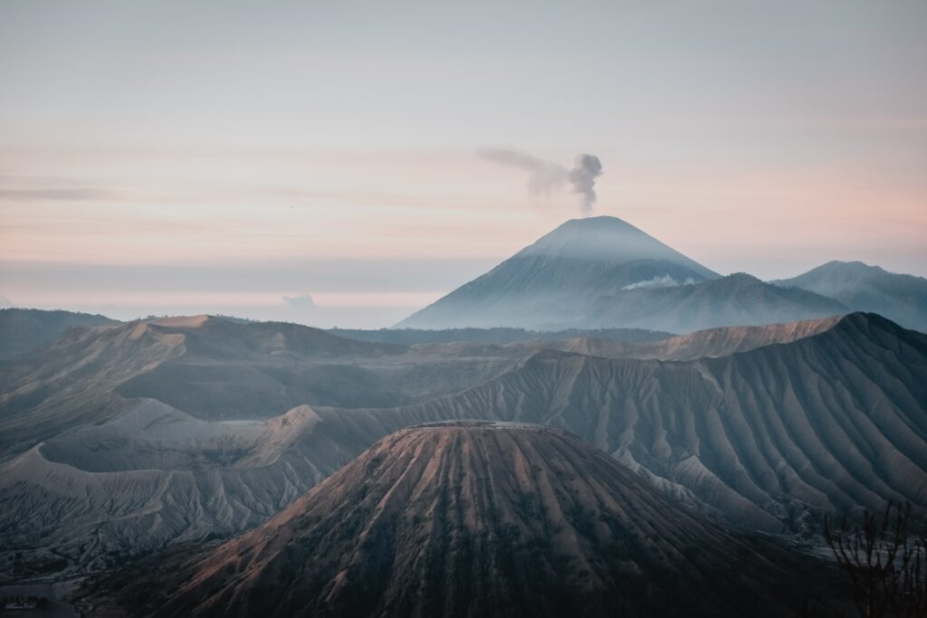 Sunrise over volcanic peak with smoke rolling misty ridges cratered terrain wallpaper background