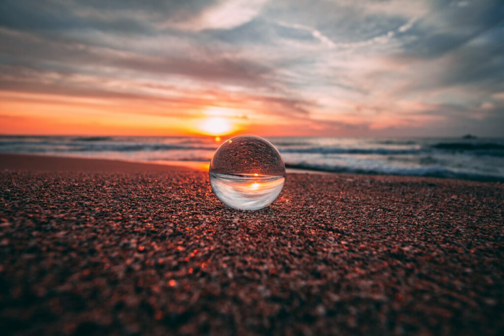 Serene Sunset Reflection Wallpaper: Glass Ball on Sandy Shore