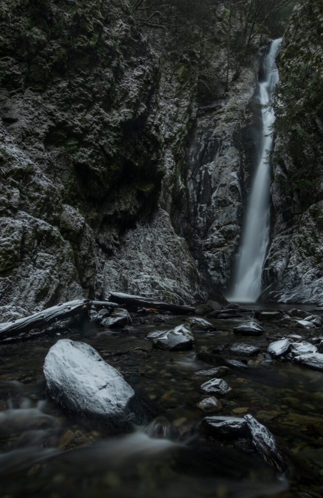 Serene waterfall cascading over rugged rocks into clear stream with lush mossy natural scenery Wallpaper