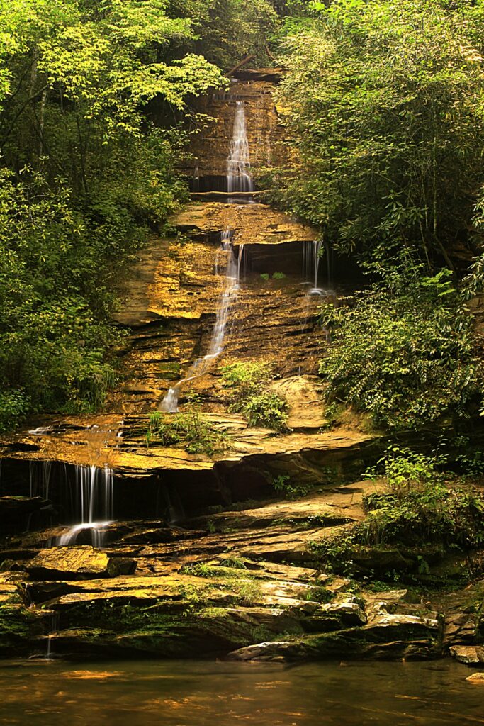 Serene waterfall cascading over layered rocks with lush green trees and vibrant foliage background Wallpaper