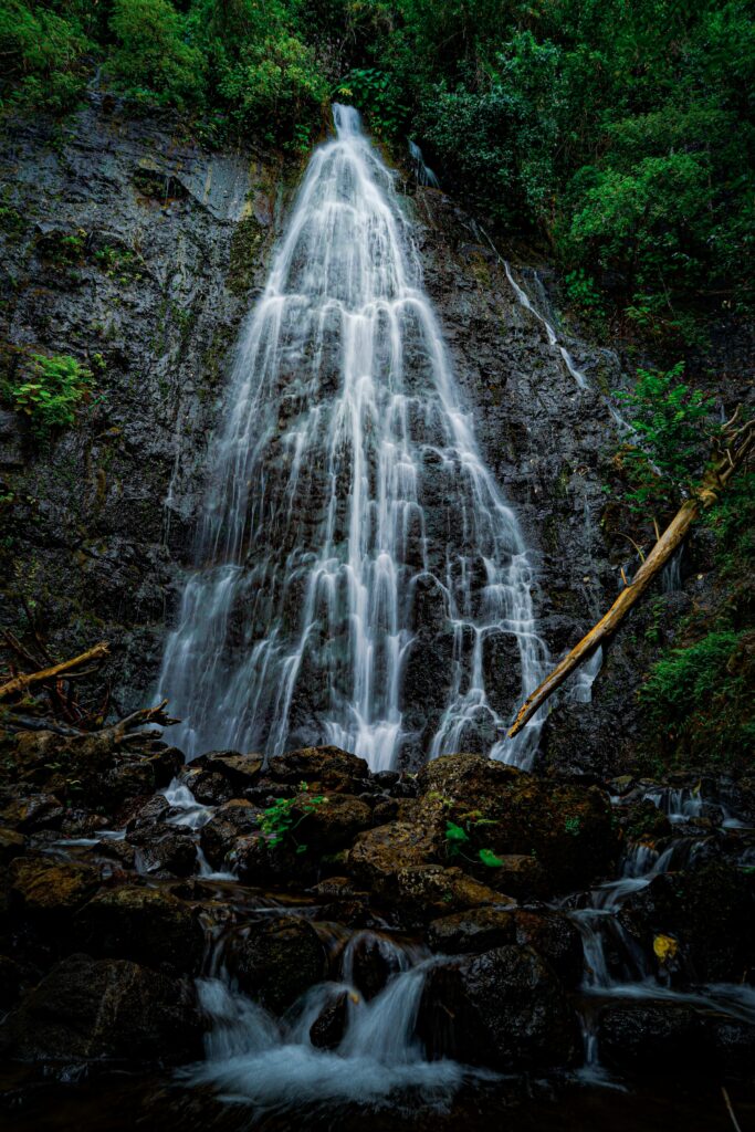 Waterfall cascading over rugged cliff surrounded by lush greenery and clear flowing stream Wallpaper