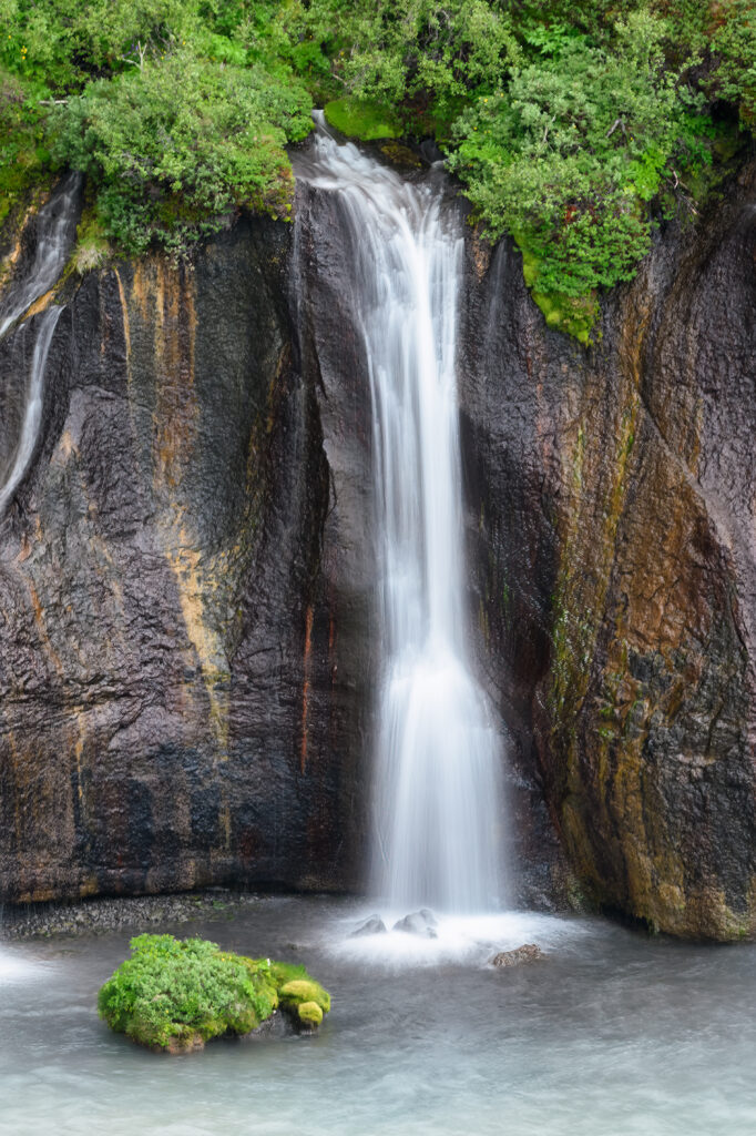 Serene waterfall flowing over rugged rocks and vibrant cliff surrounded by lush green forest Wallpaper