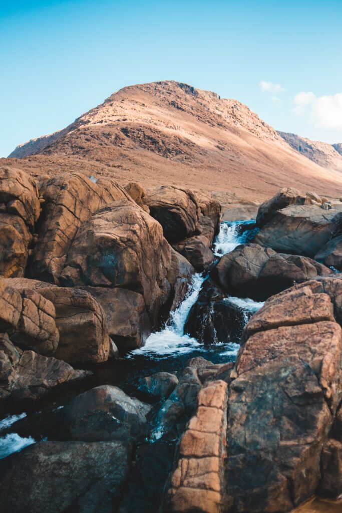 Serene waterfall cascading over rugged rocks below towering mountain under clear blue sky wallpaper