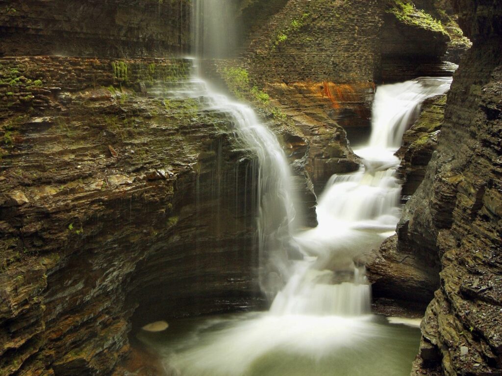 Serene gorge with cascading waterfalls over mossy rocks into clear pool lush tranquil landscape Wallpaper