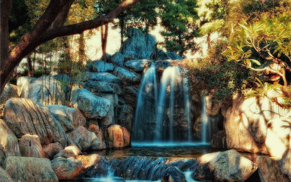 Serene waterfall cascading over rocks into calm river surrounded by lush green trees HDR wallpaper