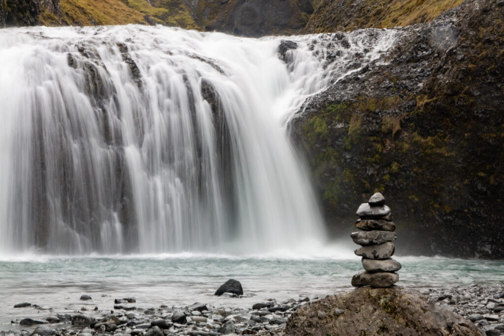 Serene waterfall cascading over dark rocks with balanced stone stack in peaceful nature scene Wallpaper
