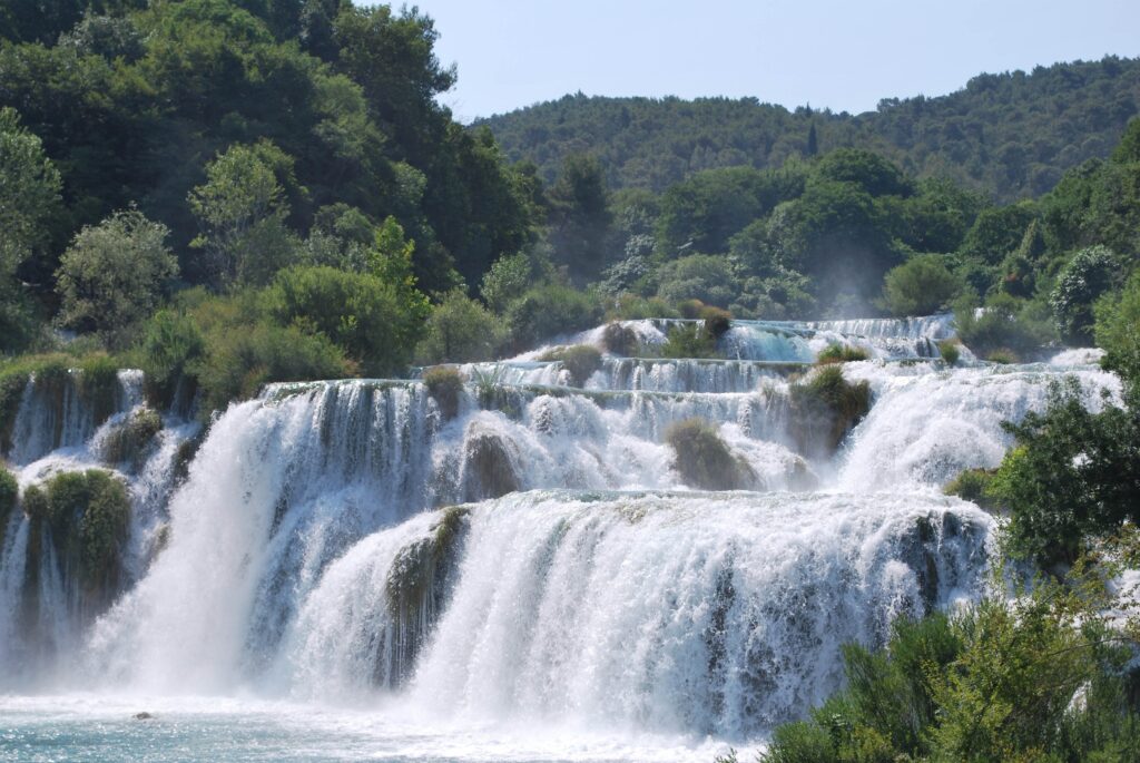 Breathtaking waterfalls flowing into clear river surrounded by lush forest vibrant foliage wallpaper