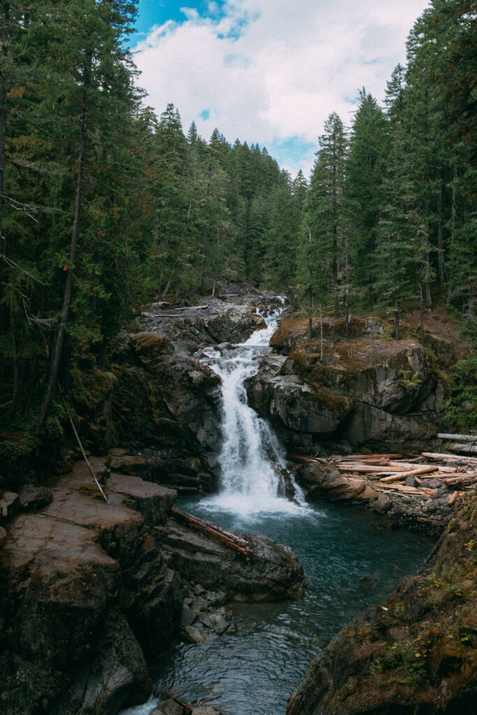 Serene waterfall cascading over rocks surrounded by dense green forest under a cloudy sky wallpaper