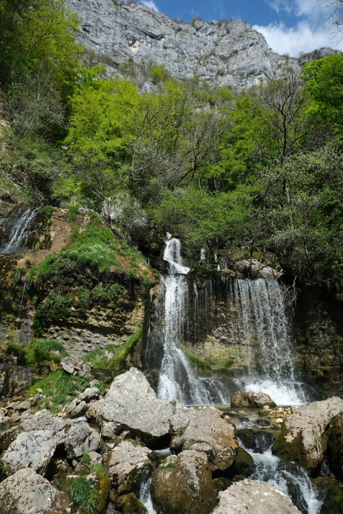 Vibrant waterfall cascading over rocks with lush green trees and dramatic cliff nature wallpaper