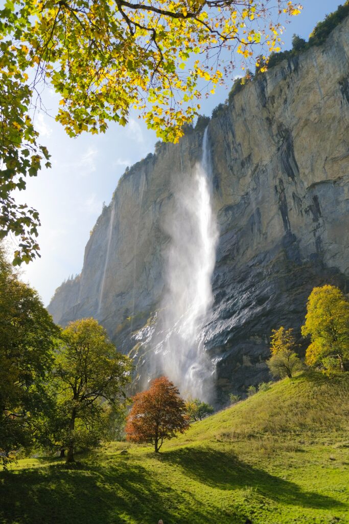 Waterfall cascading over rocky cliffs surrounded by lush green trees and sunlight beams Wallpaper