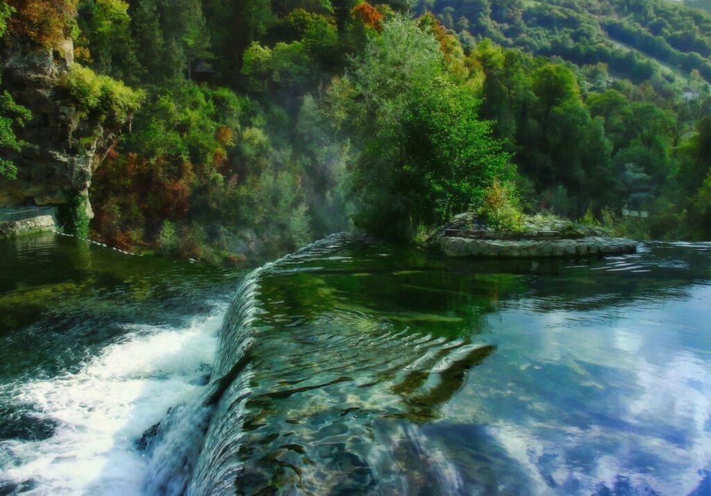 Serene river waterfall with lush trees rocky cliffs foam mist vibrant landscape wallpaper background