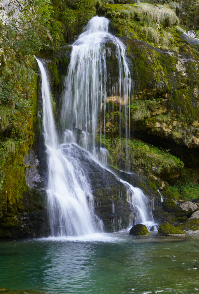 Serene waterfall flowing over mossy stones into emerald pool surrounded by lush greenery wallpaper