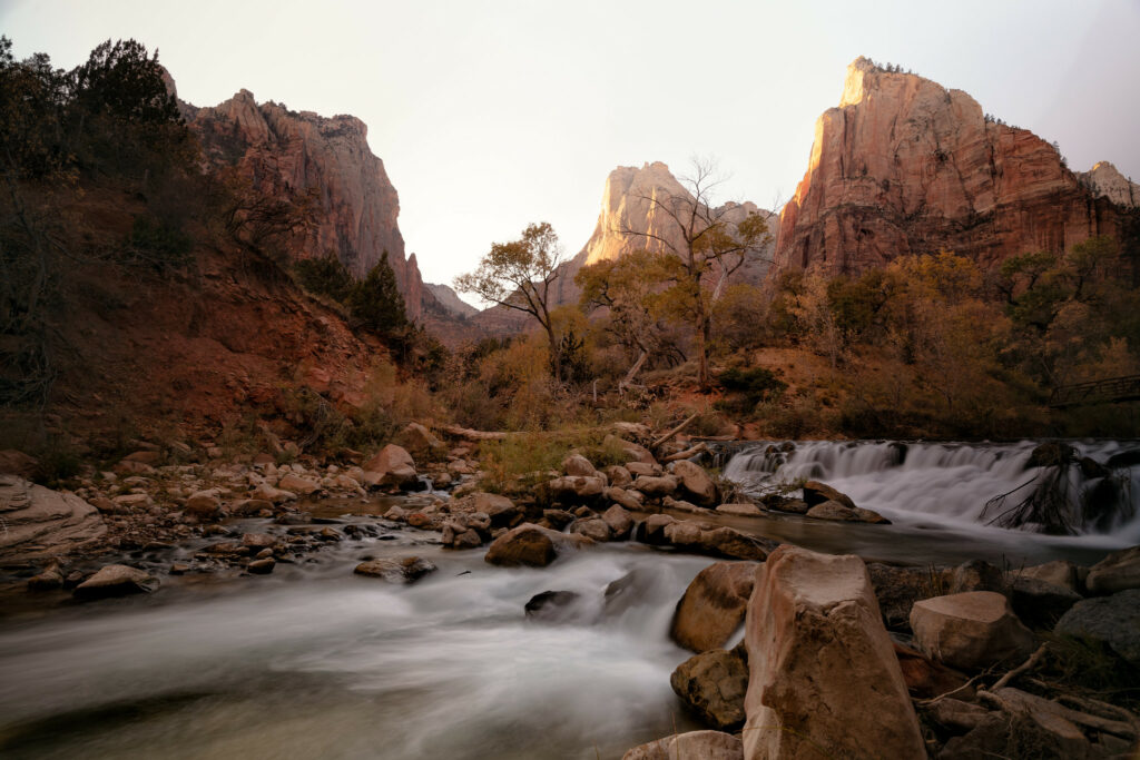 Serene waterfall and stream surrounded by rocks lush trees and sunlit cliffs nature wallpaper