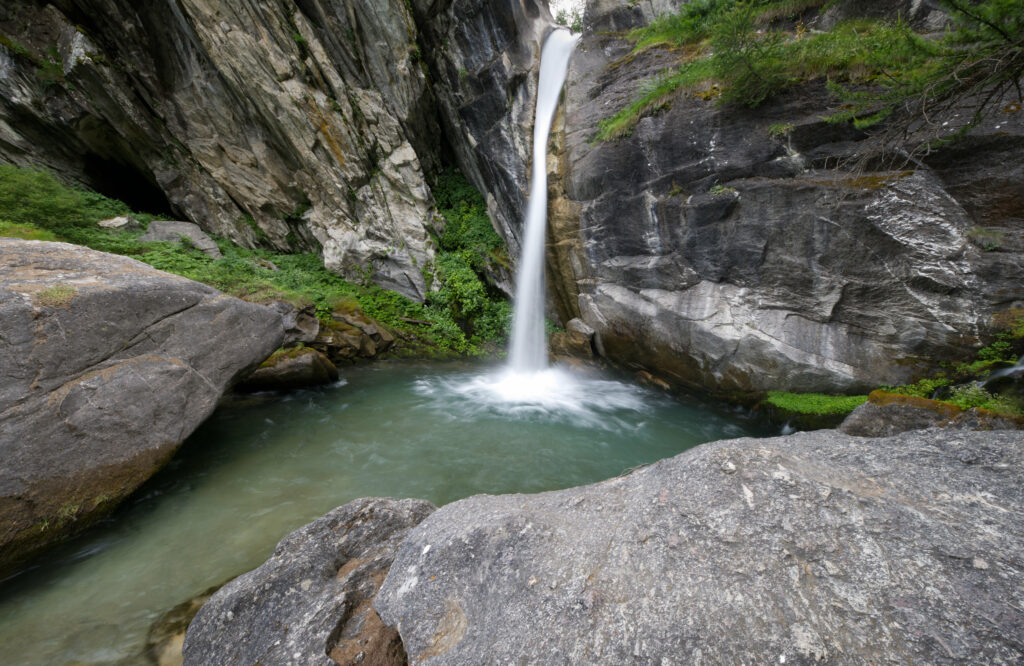 Serene waterfall cascades down stone cliffs into a clear pool surrounded by lush greenery wallpaper