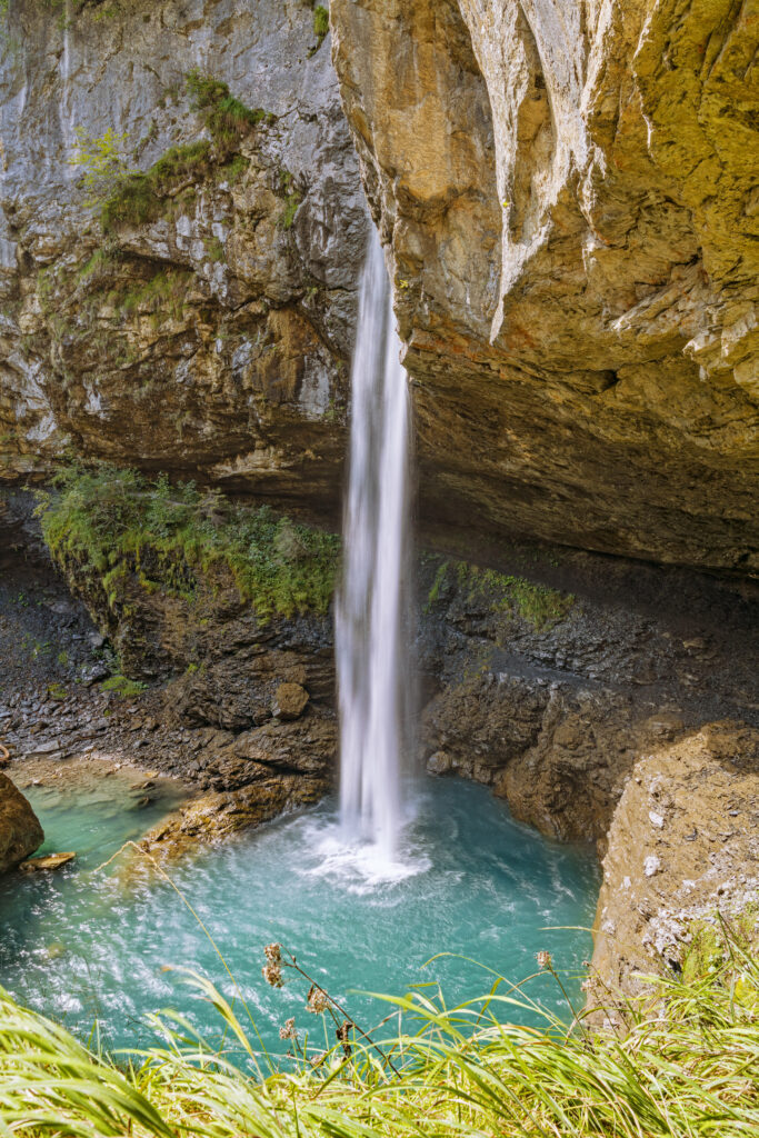 Waterfall cascading from rocky cliffs into turquoise pool surrounded by lush green grass wallpaper