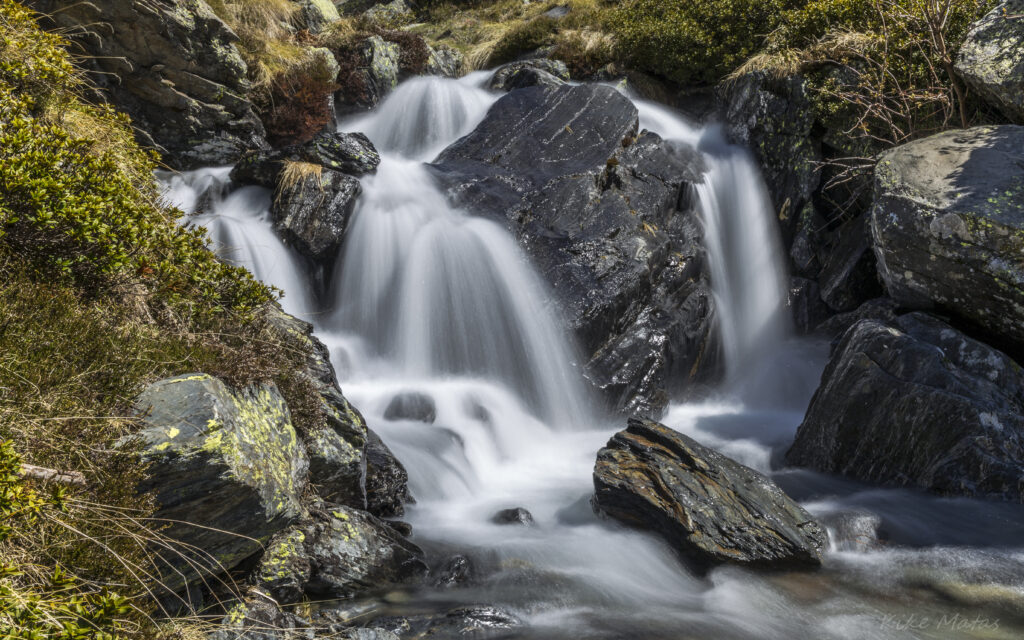 Serene waterfall flowing smoothly over rugged stones in lush landscape long exposure wallpaper