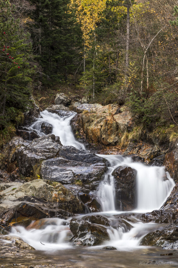 Serene waterfall flowing over smooth stones with silky water and autumn foliage wilderness wallpaper