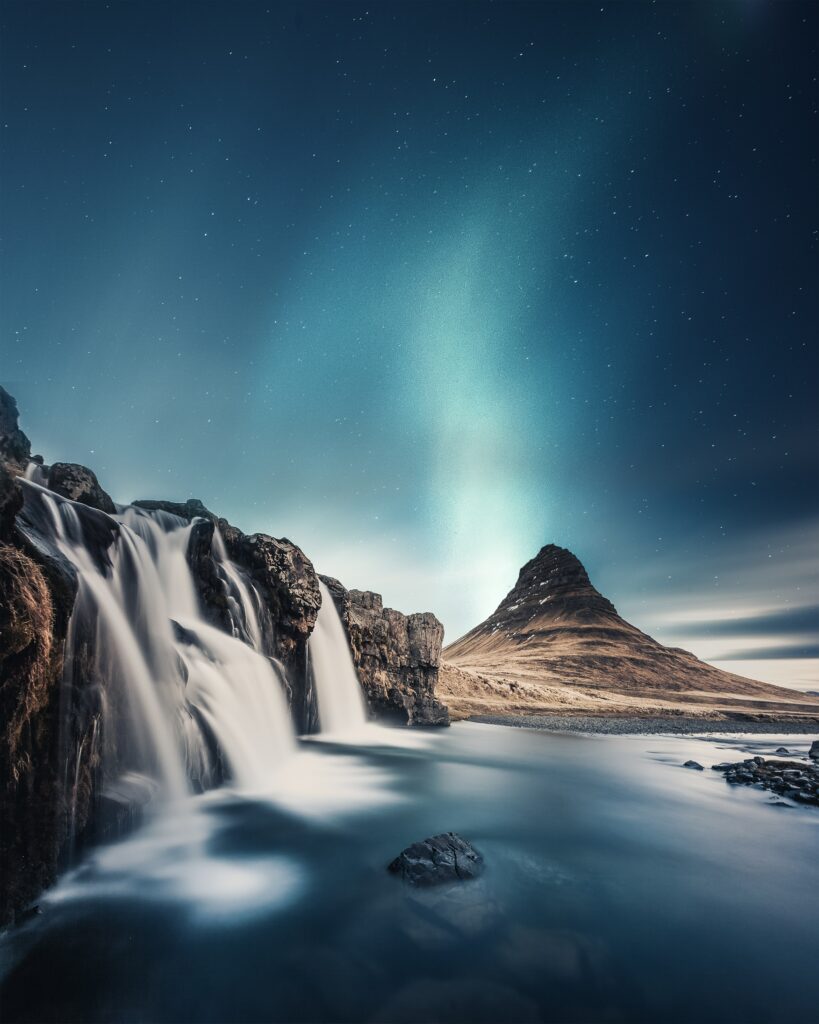 Waterfall cascading over smooth stones into river at night with mountains and starry sky wallpaper