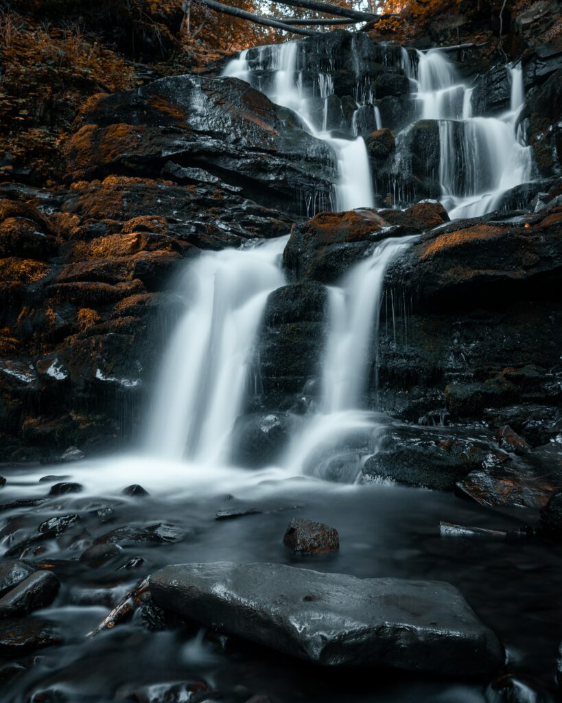 Silky smooth waterfall cascading over dark rocks with misty spray and serene stream background Wallpaper