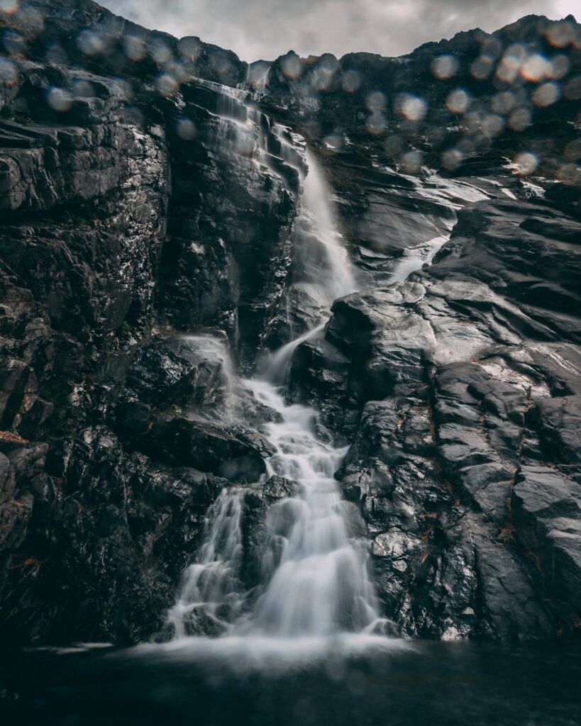 Waterfall cascading over dark stones with soft light glare and bokeh for serene nature scene Wallpaper