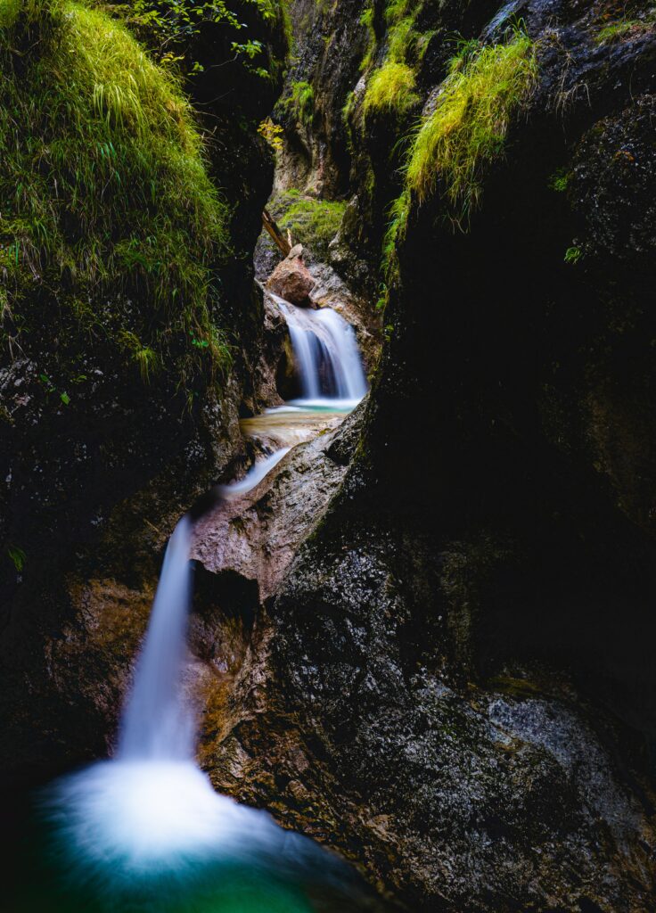 Serene waterfall over dark rocks with clear stream and lush green grass in tranquil wilderness Wallpaper