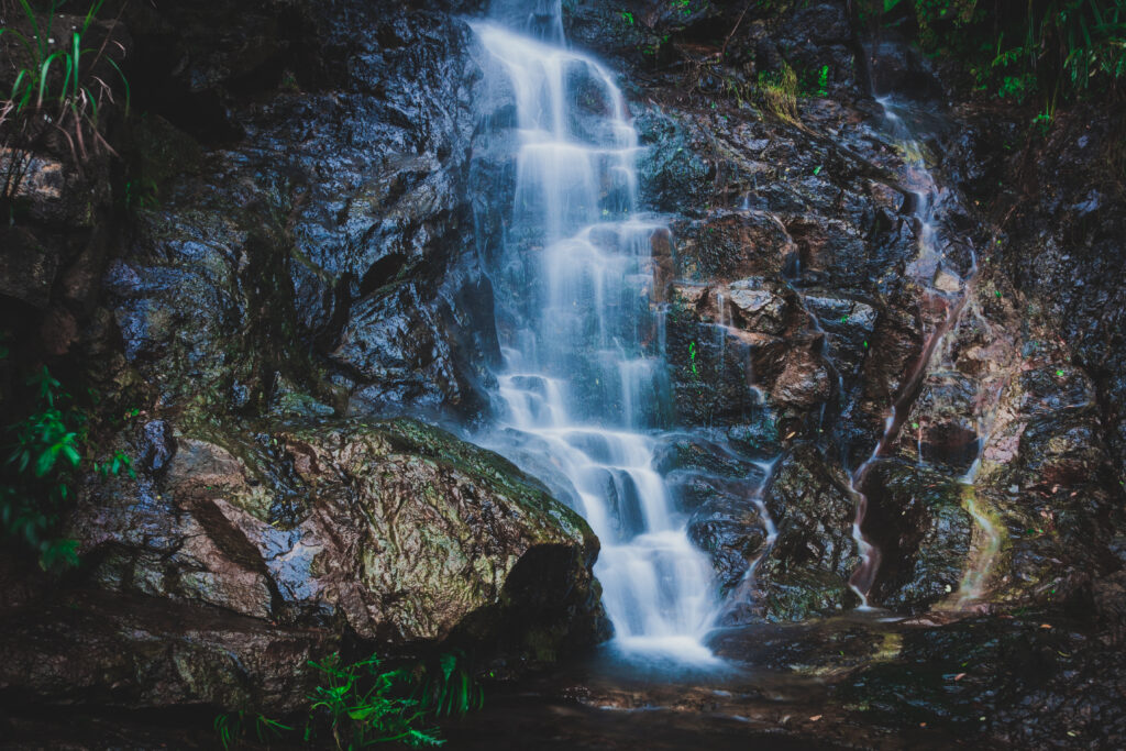 Serene waterfall cascading over dark rocks with mist and lush green foliage background wallpaper