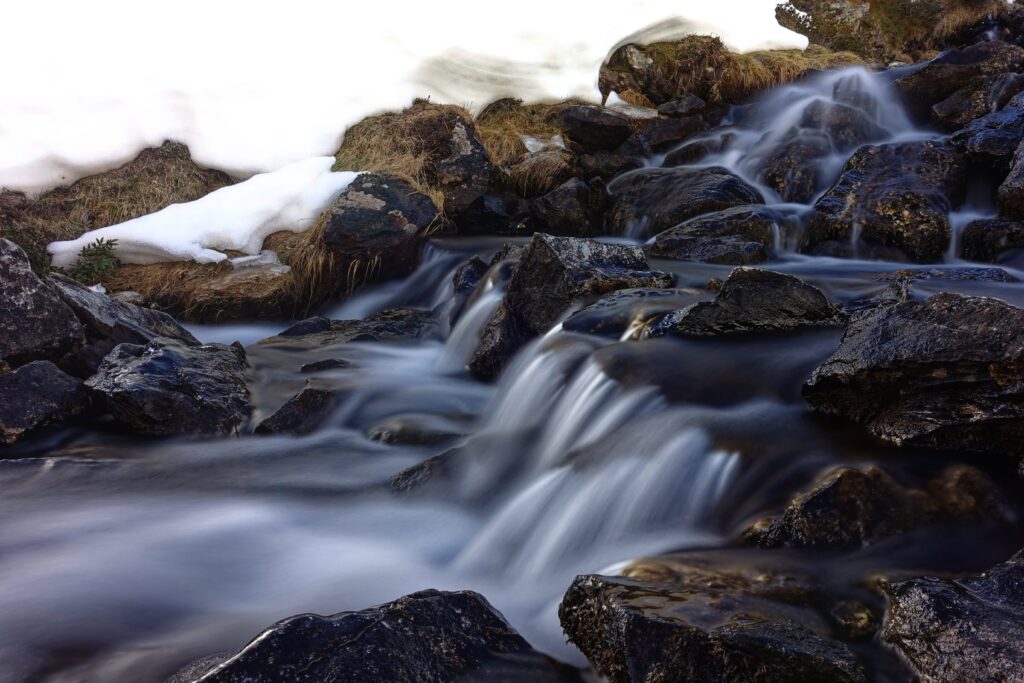 Serene waterfall over smooth dark stones with rushing rapids and snowy riverbanks wallpaper