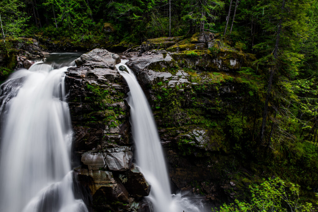 Waterfall cascading over mossy cliff into serene river surrounded by dense green forest wallpaper