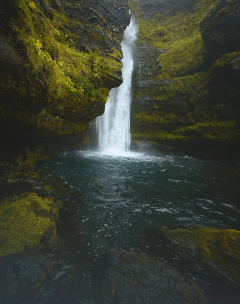 Serene waterfall cascading moss-covered cliff with clear dark basin and weathered stones wallpaper background