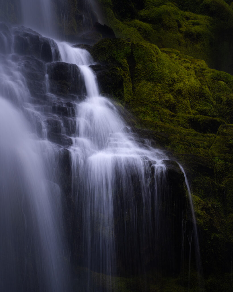 Serene waterfall cascading over mossy dark rocks nature wallpaper background for desktop