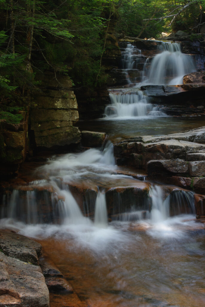 Serene waterfall cascading over stone blocks with mossy rocks and lush green forest background Wallpaper
