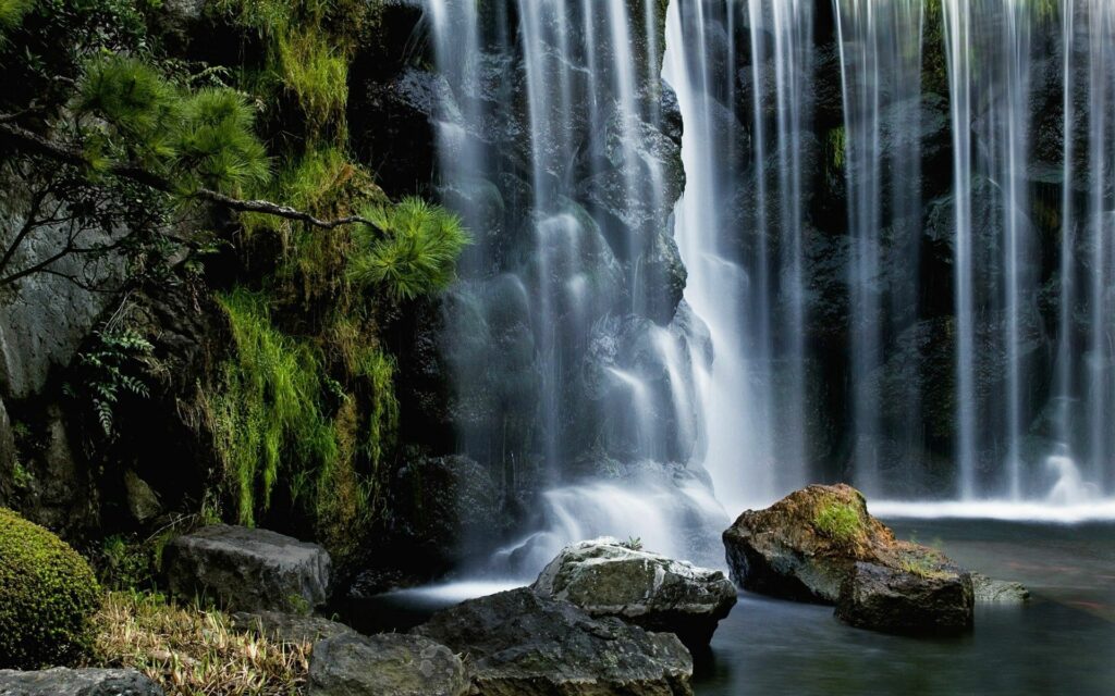 Serene waterfall cascading over rugged stones surrounded by lush green moss and vegetation Wallpaper