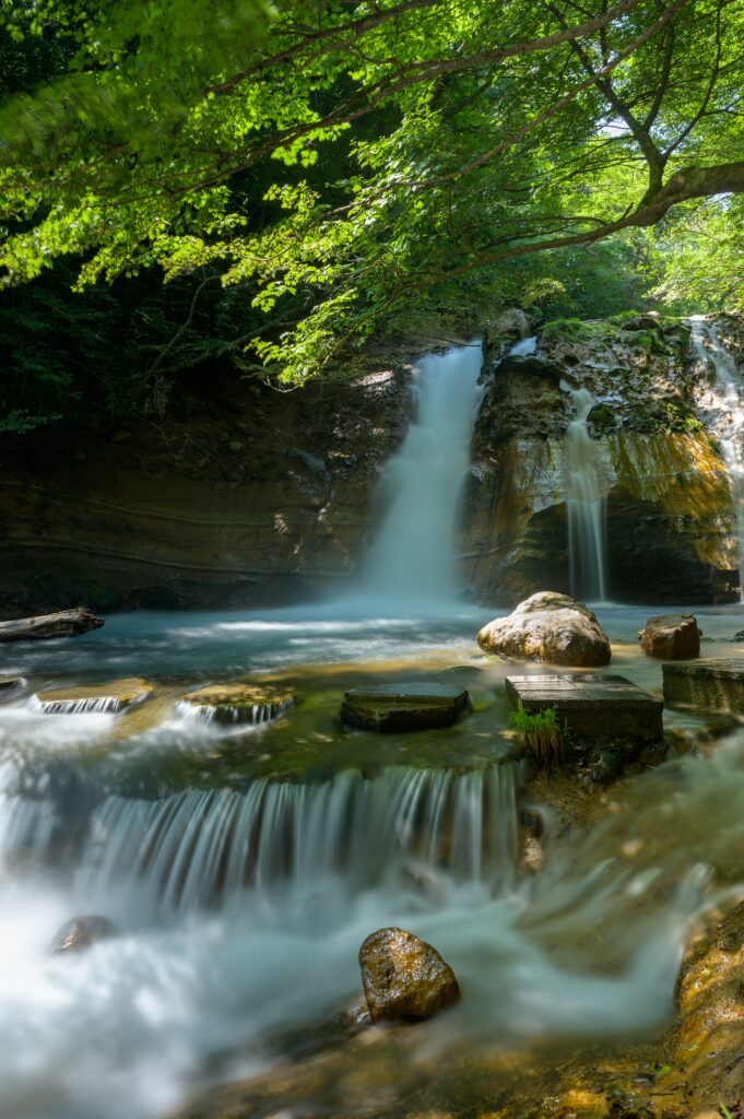 Serene waterfall cascading over stones with lush trees and sunlight mist peaceful nature wallpaper