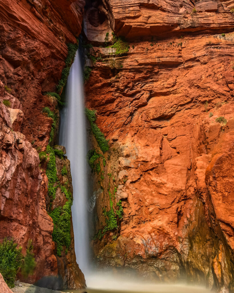 Waterfall cascading down red rock cliffs with green moss creating serene natural scenery wallpaper