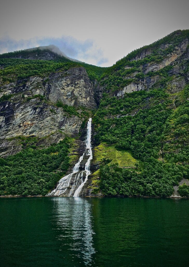 Serene waterfall cascading down rocky cliffs into calm lake surrounded by vibrant green foliage wallpaper