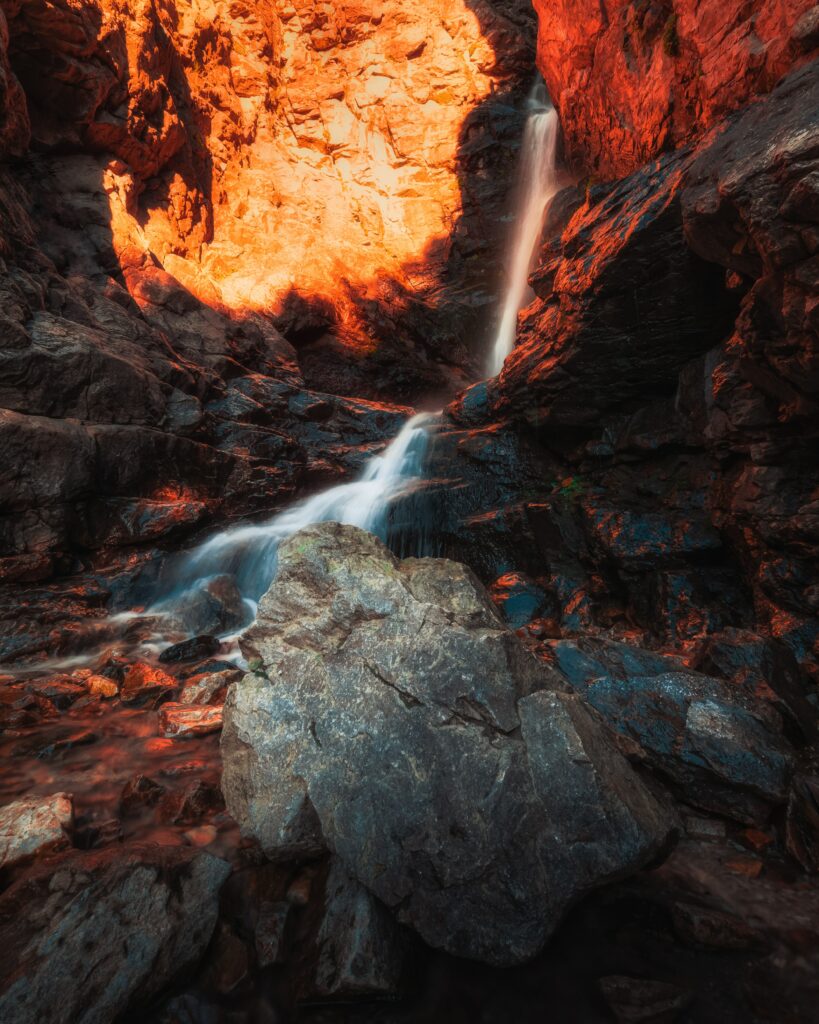 Serene waterfall flowing over rocky terrain in warm sunlight with vivid earthy tones background Wallpaper