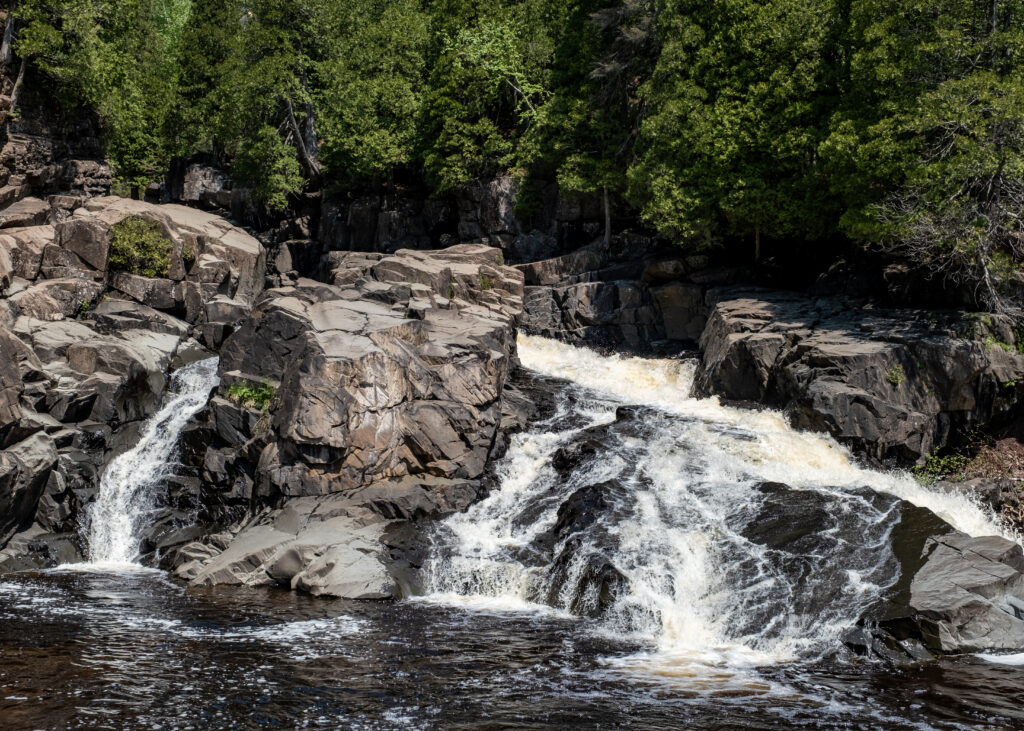 Cascading waterfall over rugged stones surrounded by lush green trees in serene forest wallpaper