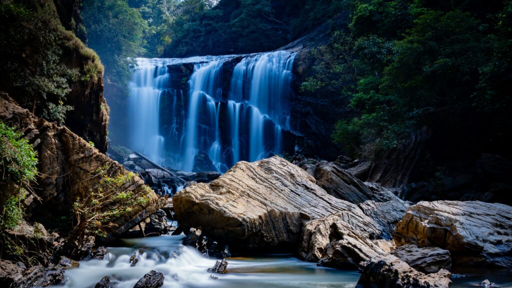 Serene waterfall flowing over rugged stones with lush green foliage for calming nature wallpaper