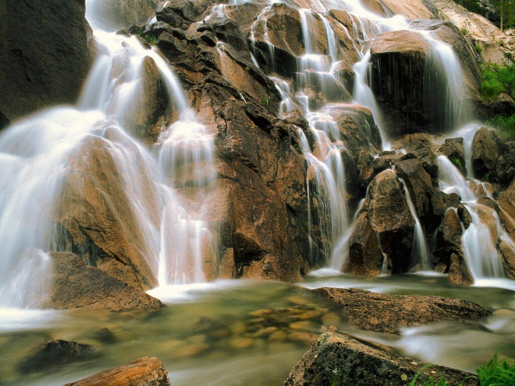 Serene waterfall cascading over rugged stones with lush green vegetation natural wallpaper background