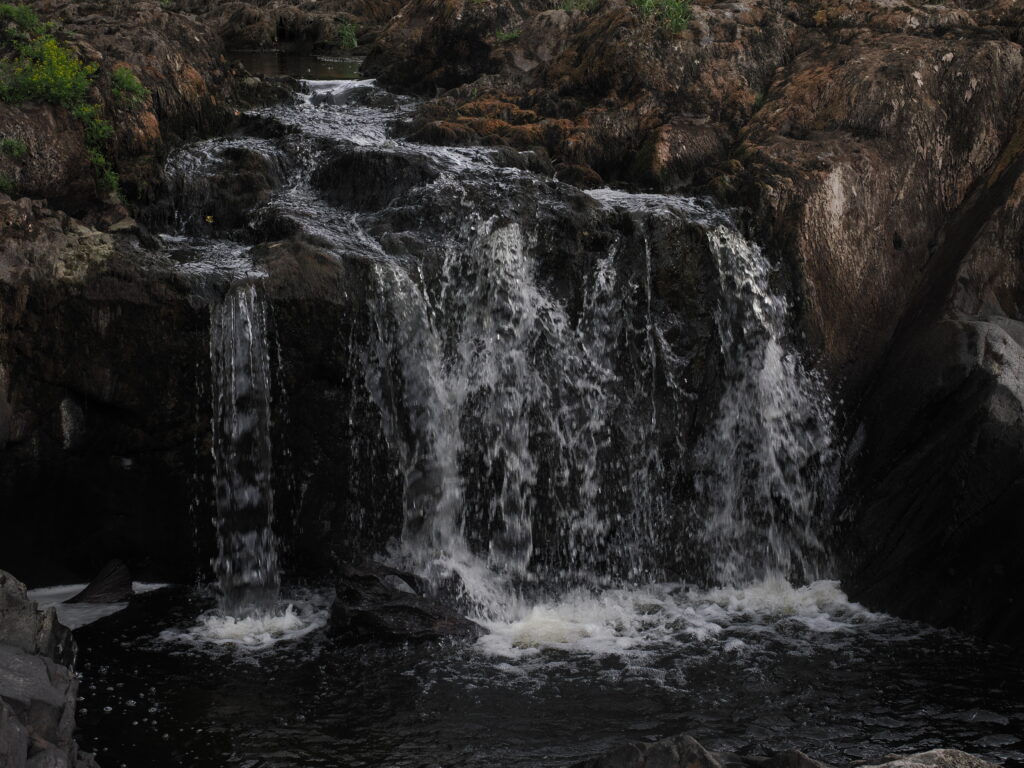 Serene waterfall cascading over rugged stones surrounded by lush greenery nature wallpaper background