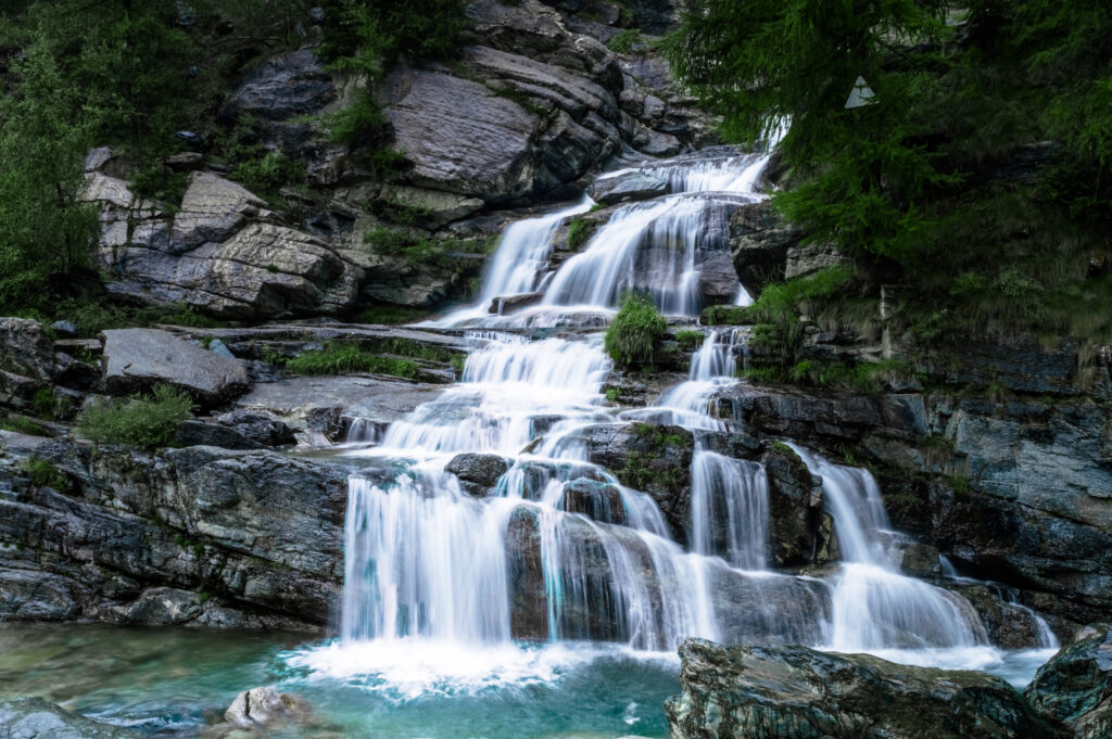 Serene waterfall cascading over rugged rocks surrounded by lush greenery and clear flowing water Wallpaper